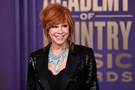 Reba McEntire smiles in a black sparkly blazer and a large decorative necklace.