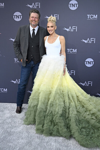 Blake Shelton and Gwen Stefani standing on a carpet smiling for photographers