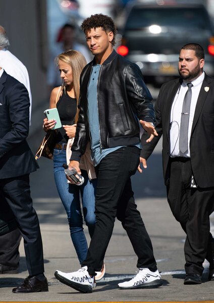 Patrick Mahomes outdoors in a black jacket, blue shirt, black pants and white sneakers.