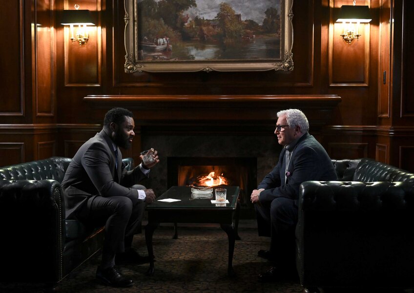 Dustin Atwood and Judge Haynes sitting across each other in a dimly lit room with wooden walls.