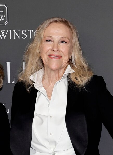 Catherine O'Hara smiles in a white shirt and black sweater.