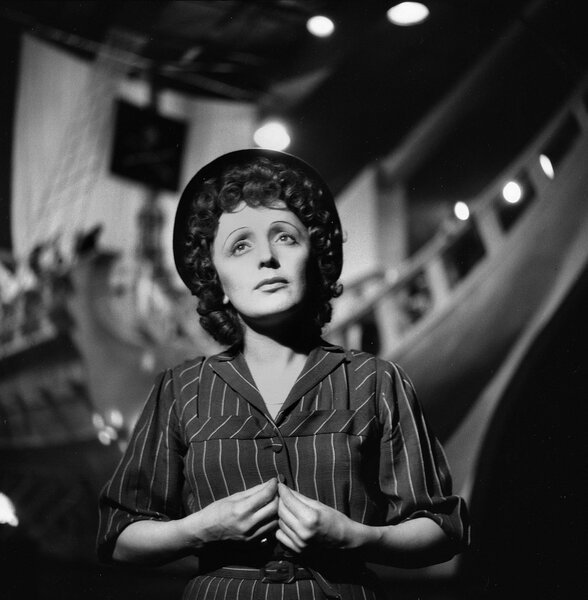 Edith Piaf standing in a costume in front of a ship.