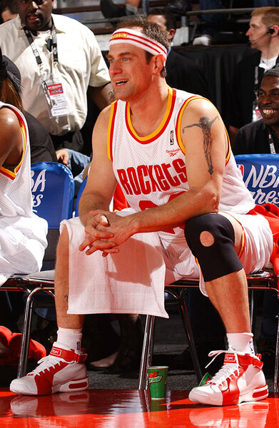 Chris Meloni sitting in a basketball uniform on a bench.