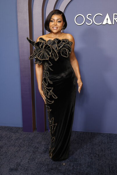 Taraji P. Henson posing in a black gown in front of a step and repeat.