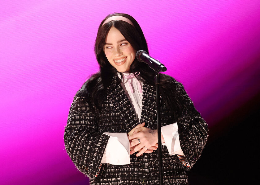 Billie Eilish performing on stage in front of a pink background.