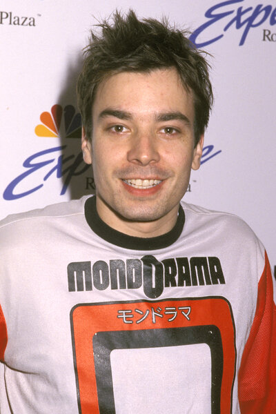 Jimmy Fallon smiles in a red and white shirt on the red carpet