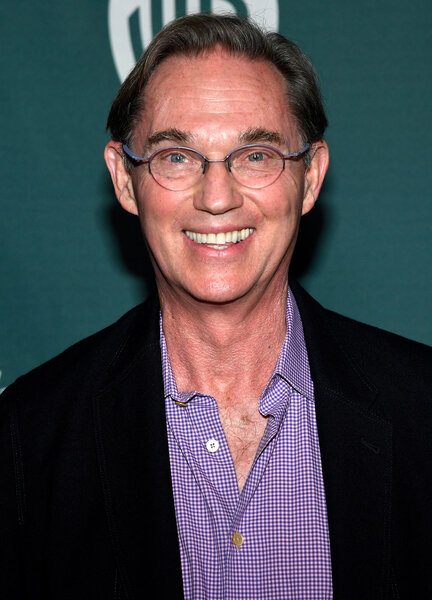 Richard Thomas smiling in front of a step and repeat.