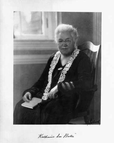 Katharine Lee Bates sits in a wooden chair near a window.