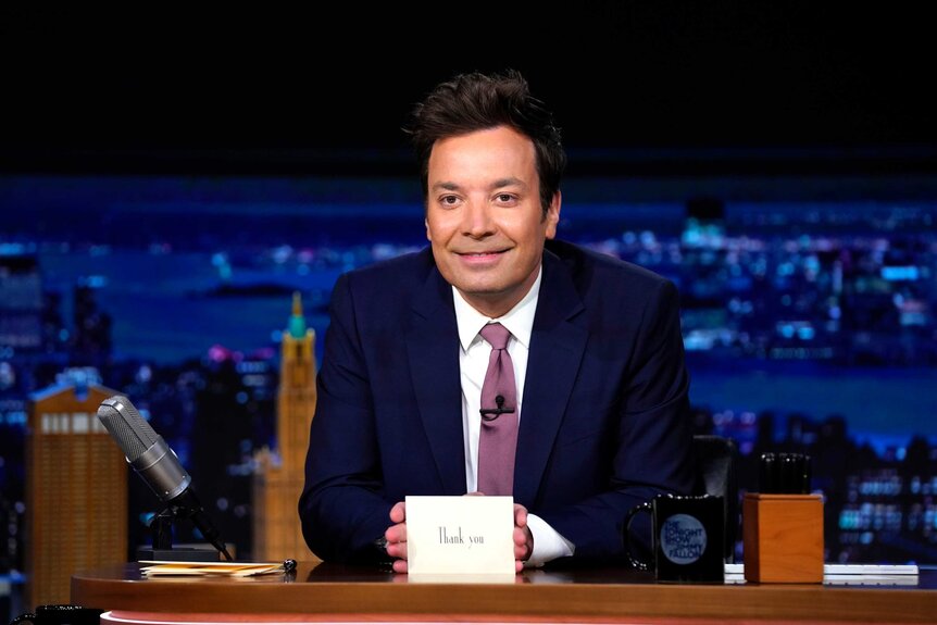 Jimmy Fallon sitting at his desk during The Tonight Show.