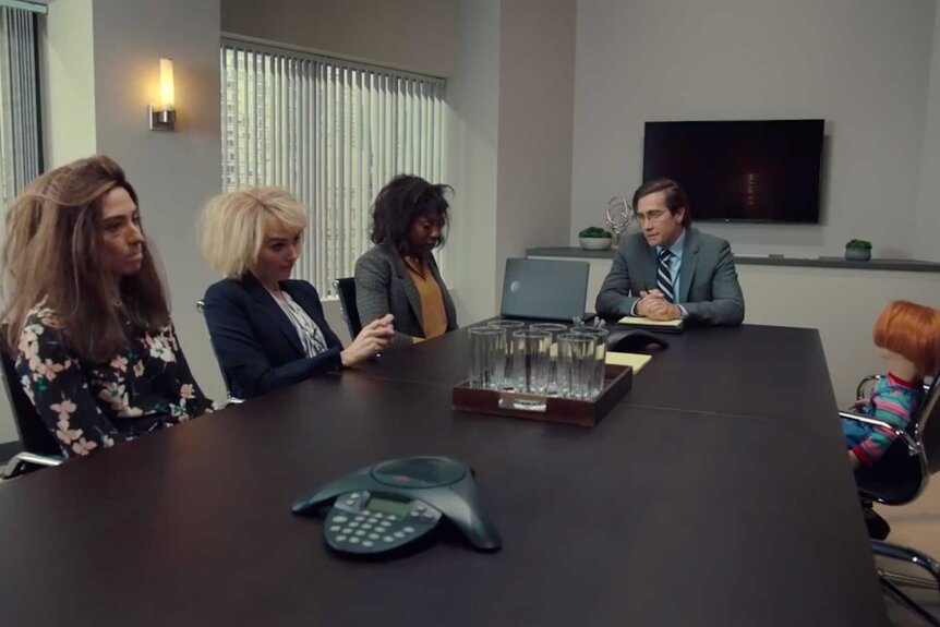 Melissa Villaseñor, Chloe Fineman, Ego Nwodim, and Jake Gyllenhaal sitting at a conference table during the Chucky sketch on Saturday Night Live.