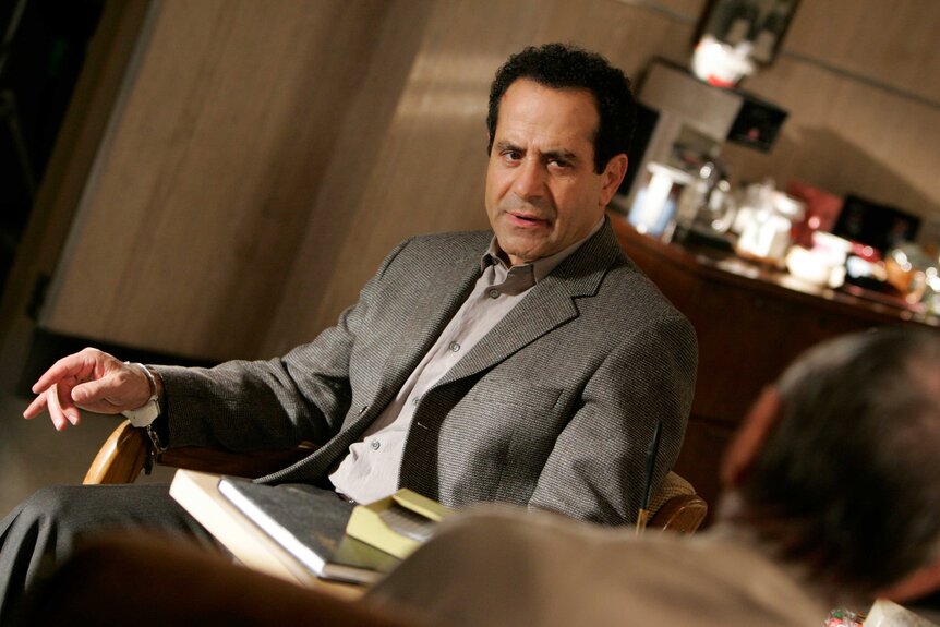 Adrian Monk in a gray suit sitting down looking off to the side.