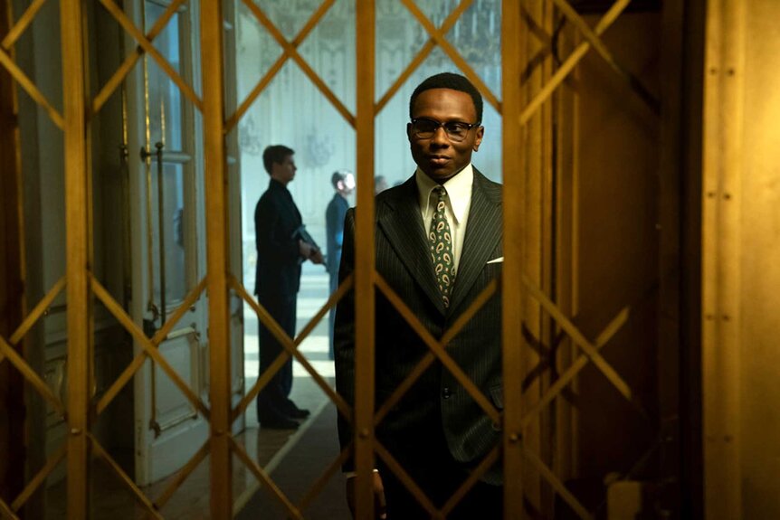 Charon standing behind an elevator during a scene from The Continental.