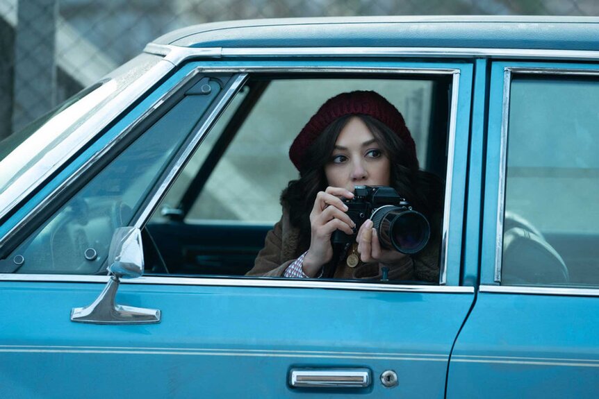 KD appears taking photos in a blue car during a scene from The Continental.