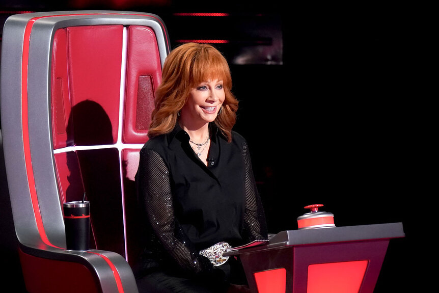 Reba McEntire sits smiling in her coach's chair