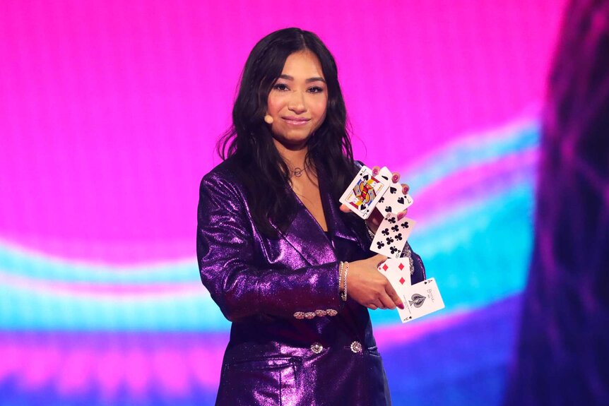 Anna Deguzman, wearing a purple blazer, shuffling playing cards in her hand on stage.