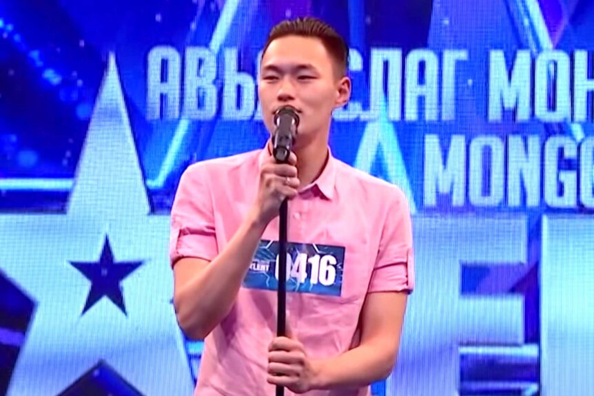 Enkh Erdene on stage, wearing a pink collared shirt, singing.