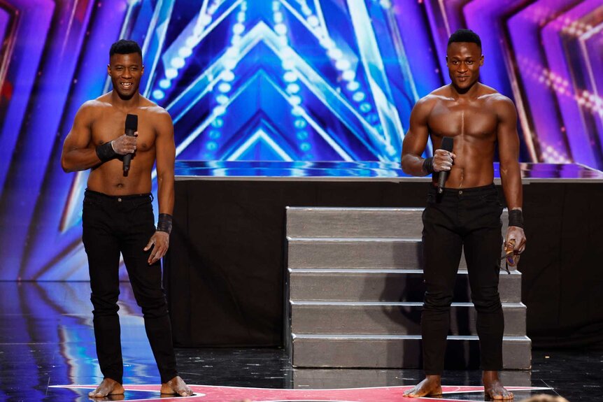 The Ramadhani Brothers holding mics in their hands on stage with a platform attached to stairs in the background.