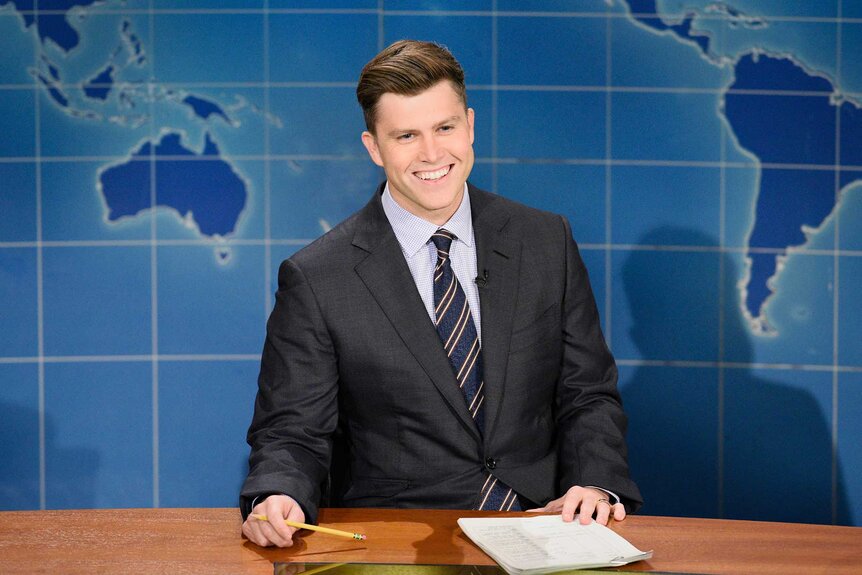 Colin Jost, wearing a gray suit, sitting at his during the Weekend Update segment.