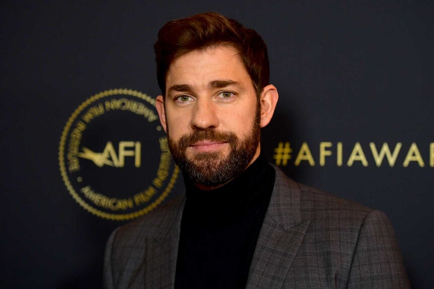 John Krasinski, wearing a brown suit, poses for the camera at the 19th Annual AFI Awards.