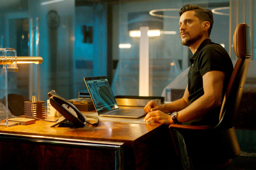 Tom Westfall sits at a desk on a computer on Quantum Leap