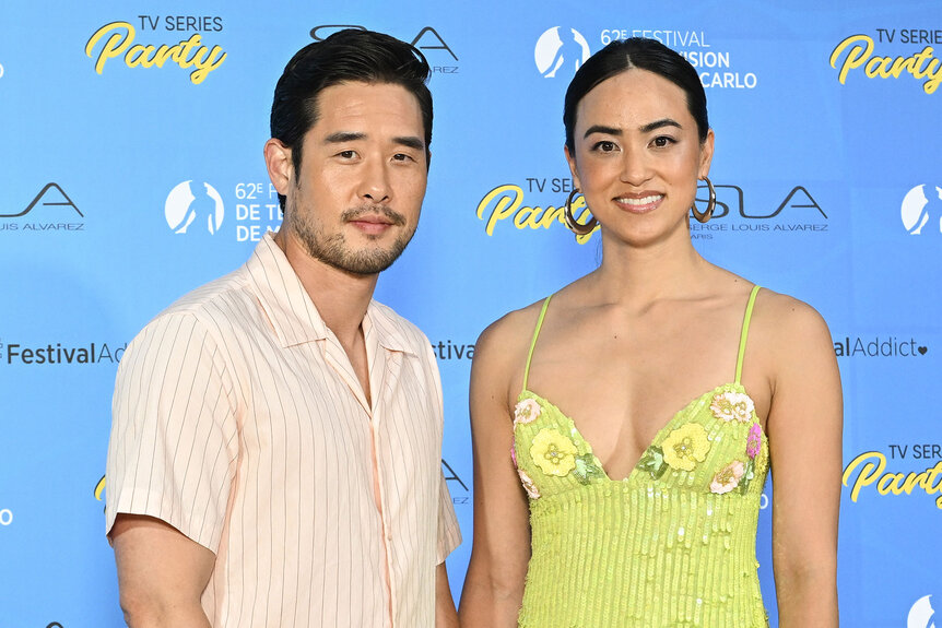 Raymond Lee stands in front of a step and repeat with his wife Stacy Kusumolku