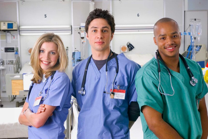 Dr. Elliot Reid, Dr. John Dorian, and Dr. Christopher Turk posing together and smiling in scrubs.