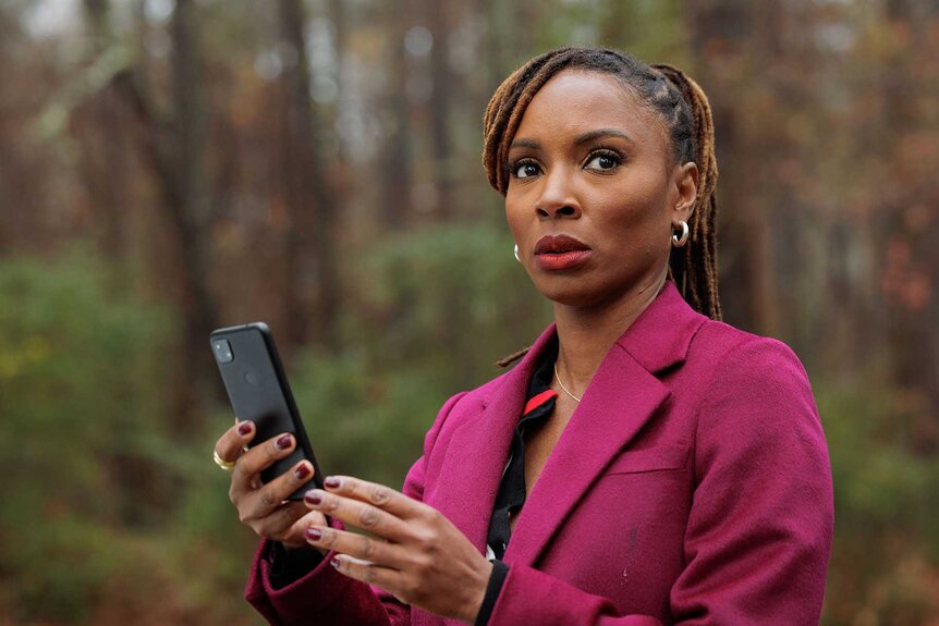 A close-up of Gabi Mosely in a magenta blazer, holding a phone while looking away.