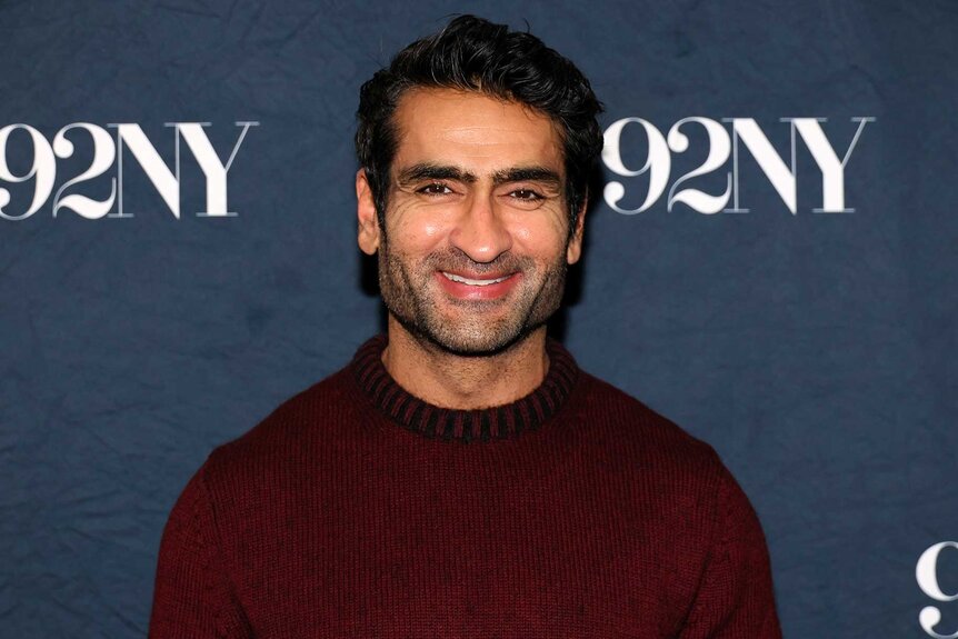 Kumail Nanjiani,wearing a burgundy top, smiling and posing for the camera