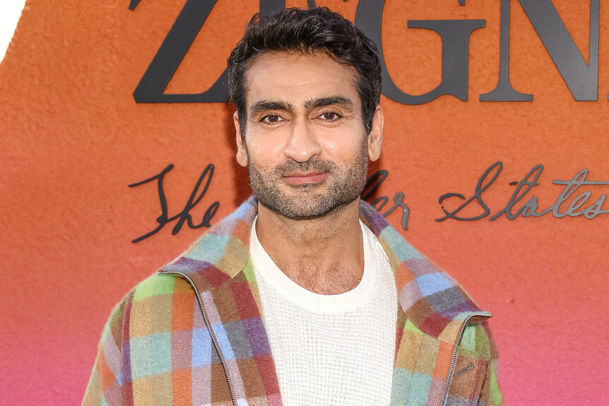 Kumail Nanjiani stands on a red carpet wearing a colorful outfit