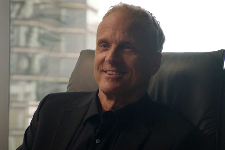 Sam Bedrosian wearing all black and sitting down at a desk in front of a bright window.