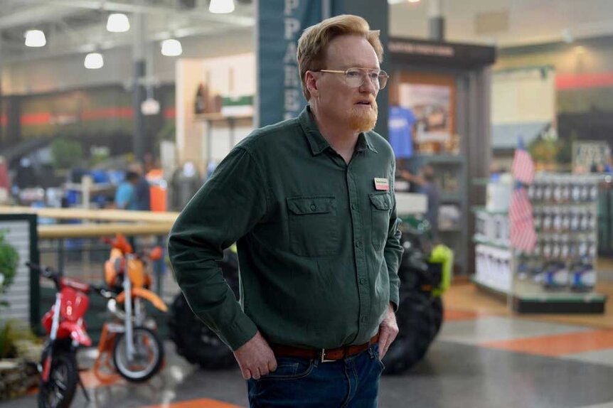 A close up of Farley wearing a green, long-sleeved shirt in a store.