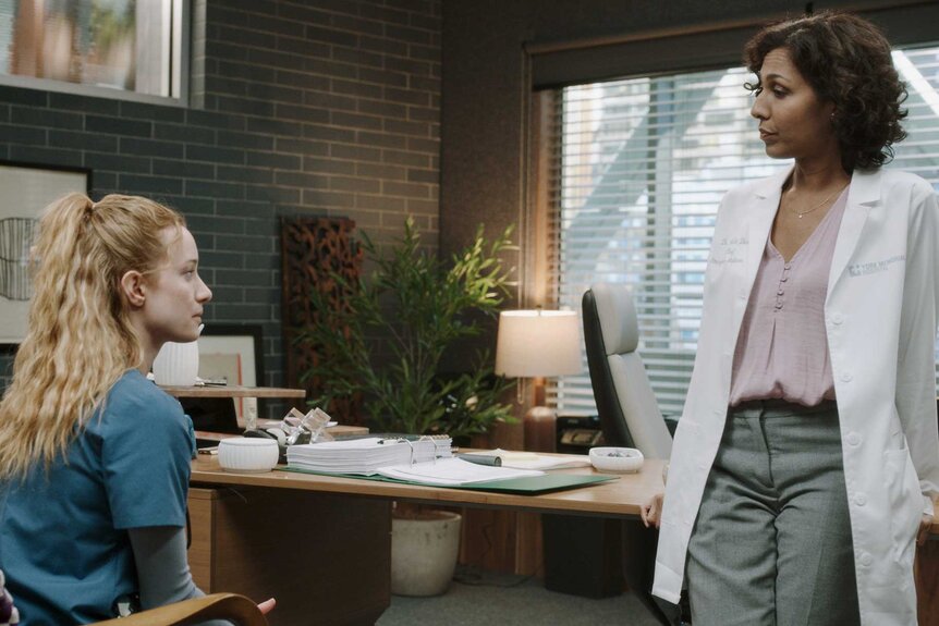 Dr. Magalie Leblanc sitting at a desk and having a conversation with another character.