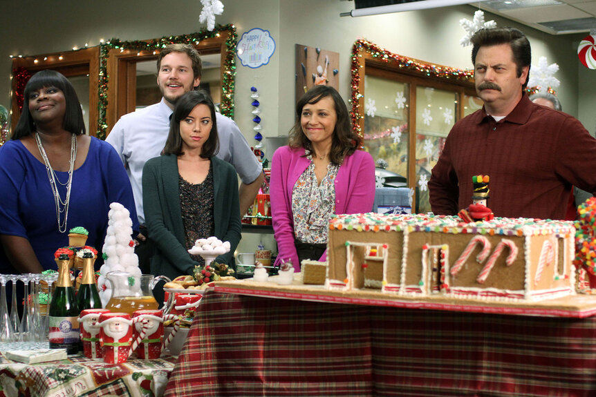 Retta (Donna), Chris Pratt as Andy Dwyer, Aubrey Plaza as April Ludgate, Rashida Jones as Ann Perkins, and Nick Offerman as Ron Swanson make gingerbread houses