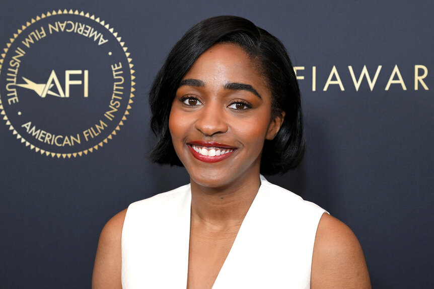 Ayo Edebiri smiles in a white dress and red lipstick at an event