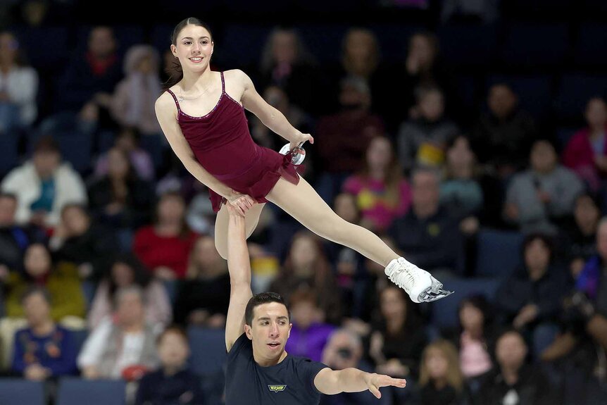 Maximiliano Fernandez holds Valentina Plazas above his head with one arm.