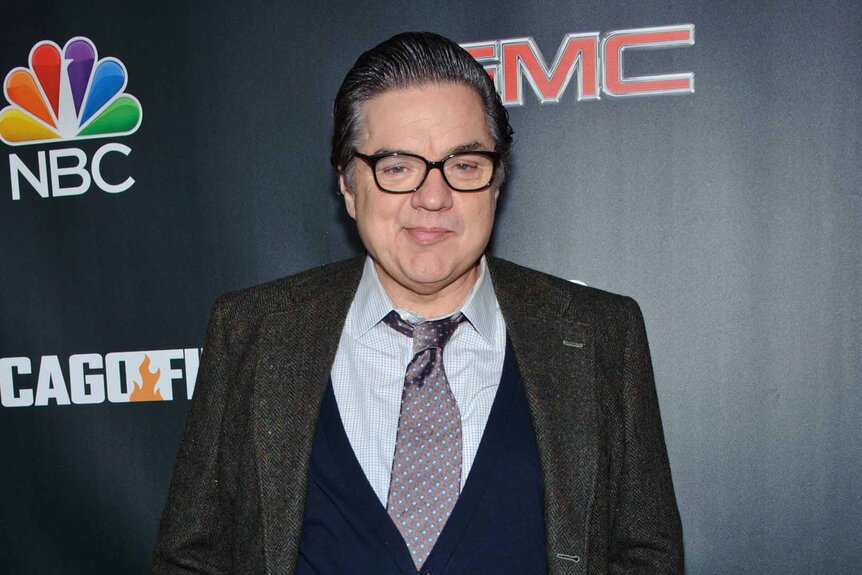 Oliver Platt smiles in a suit.