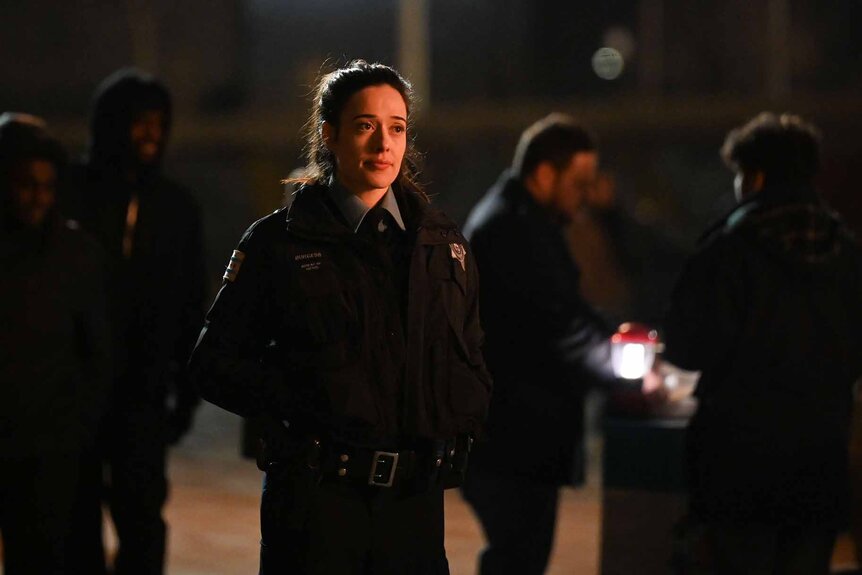 Kim Burgess stands outside at night in police uniform in Chicago P.D. 1103.