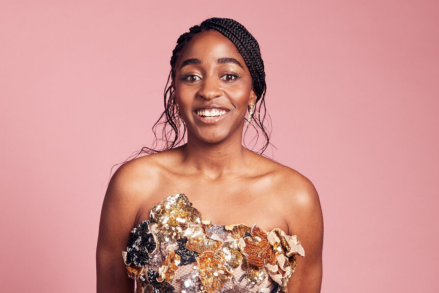 Ayo Edebiri poses in the IMDb Portrait Studio in front of a pink background smiling