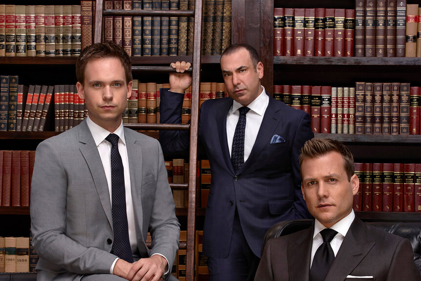 Michael Ross, Louis Litt, and Harvey Specter pose in front of bookshelves.