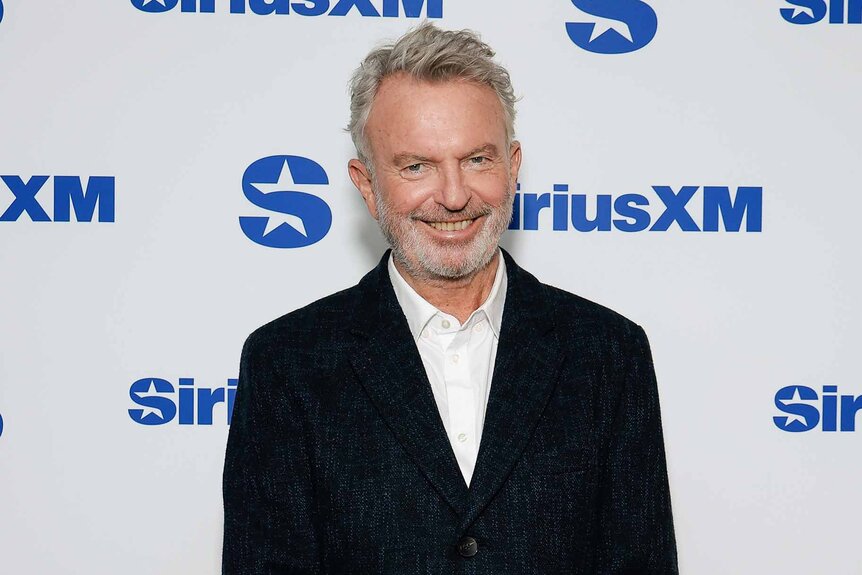 Sam Neill poses in a black jacket.