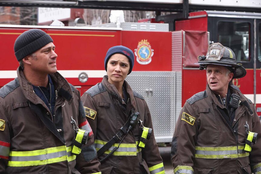 Kelly Severide , Stella Kidd, and Christopher Herrmann stand in uniform near a fire truck Season 12 Episode 8 "All the Dark".