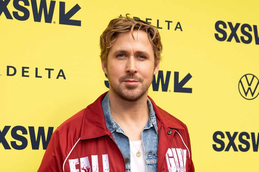 Ryan Gosling smiles in a red jacket.