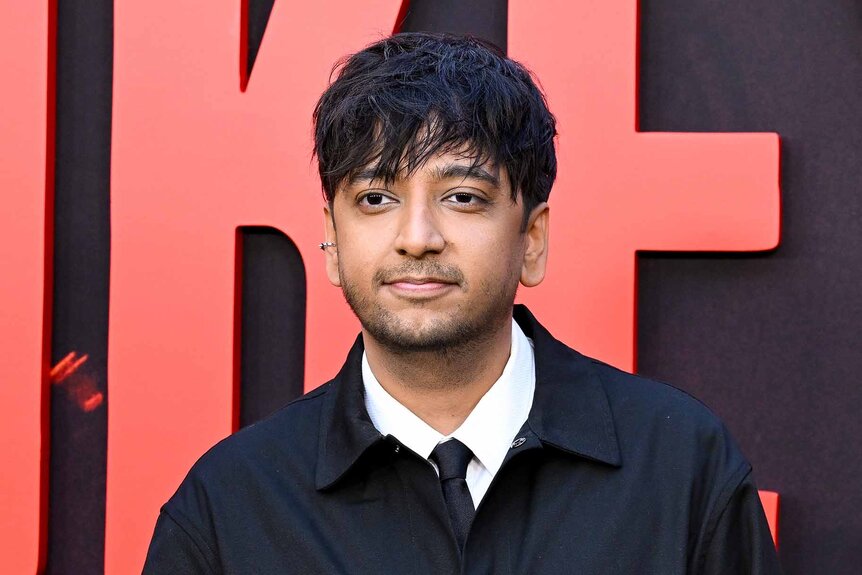 Nik Dodani smiles in a navy jacket.