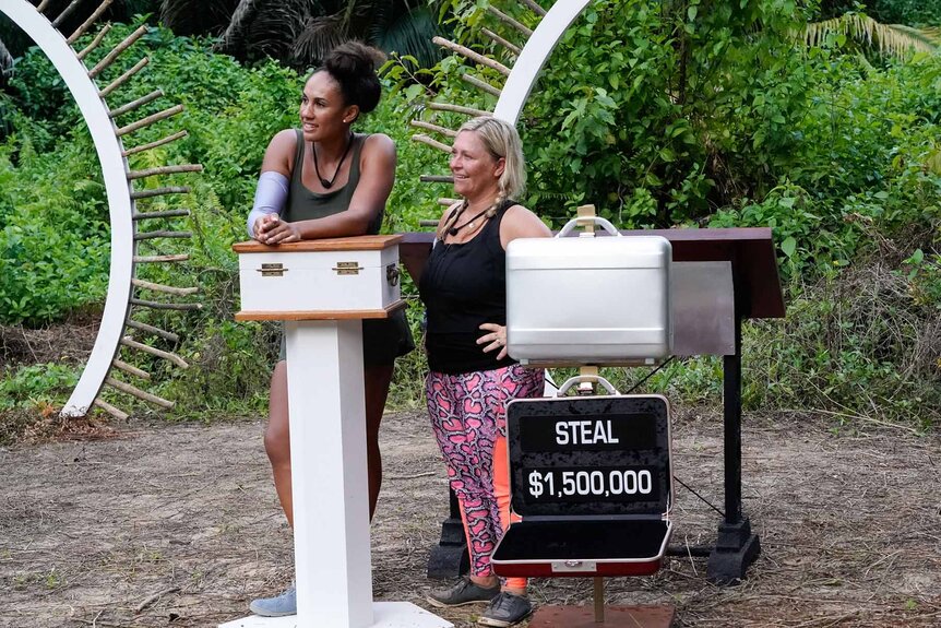 Jordan Fowler and Amy McCoy stand next to briefcases in Deal or No Deal Island Episode 109.