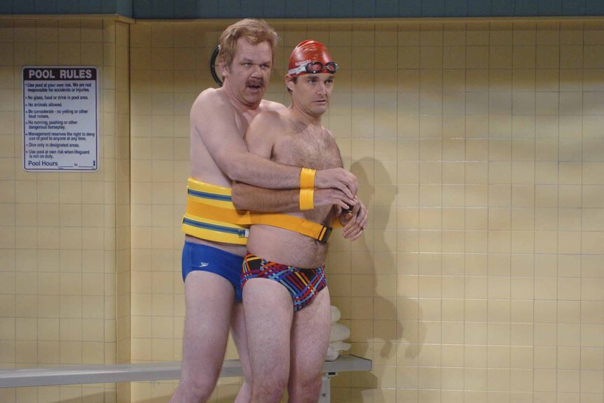 Doug Frangelo and Terry James are strapped together while wearing bikini bottoms at a pool in the Saturday Night Live skit "Swimming Lessons".