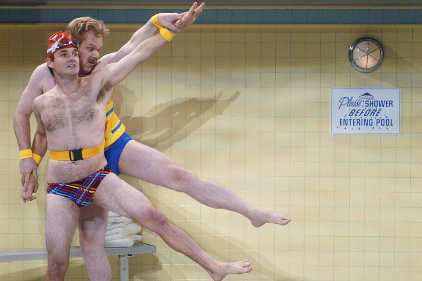 Doug Frangelo and Terry James are strapped together while wearing bikini bottoms at a pool in the Saturday Night Live skit "Swimming Lessons".