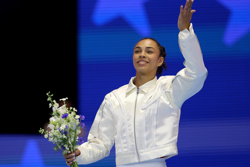 Hezly Rivera smiles while holding flowers and raising an arm up.