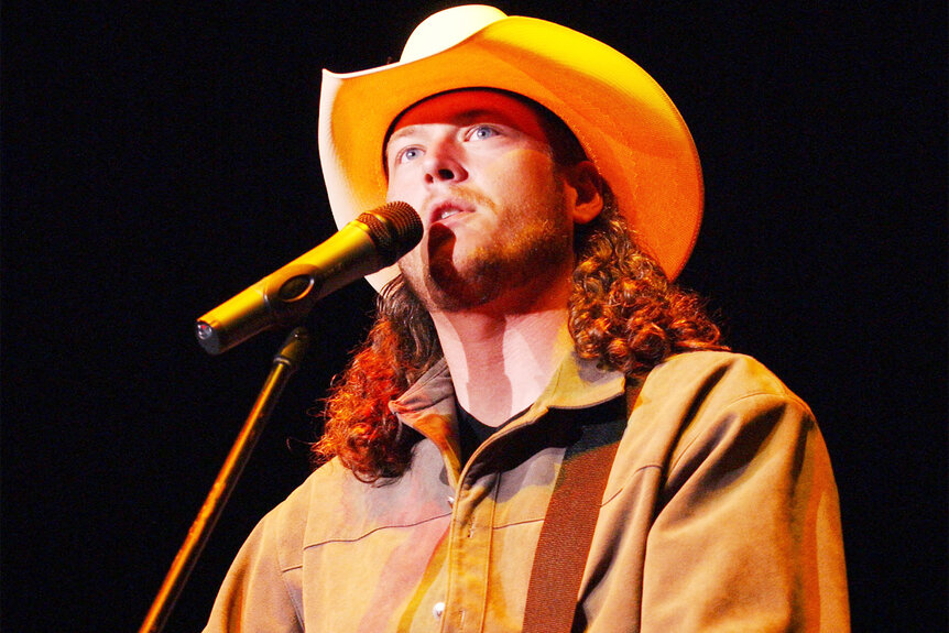 Blake Shelton performs on stage in a cowboy hat and curly long hair