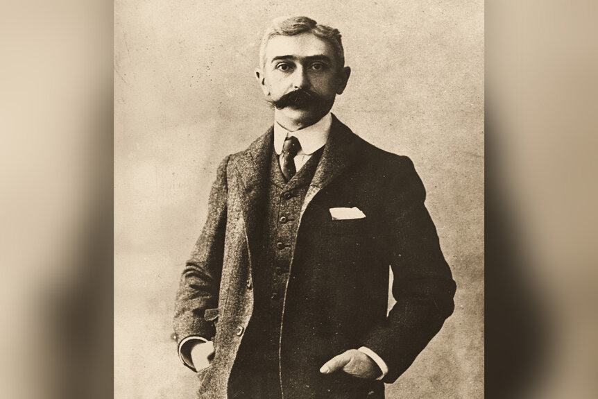 Baron Pierre Coubertin wears a suit and dons a mustache.