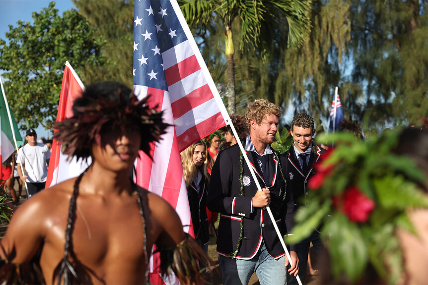 John John Florence holds the american flag at the 2024 Olympics Opening Ceremony